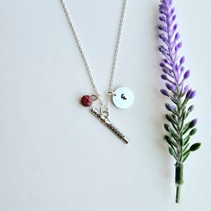 May include: A silver necklace with a silver flute charm, a small red rhinestone charm, and a silver disc charm with the letter "E" on it.