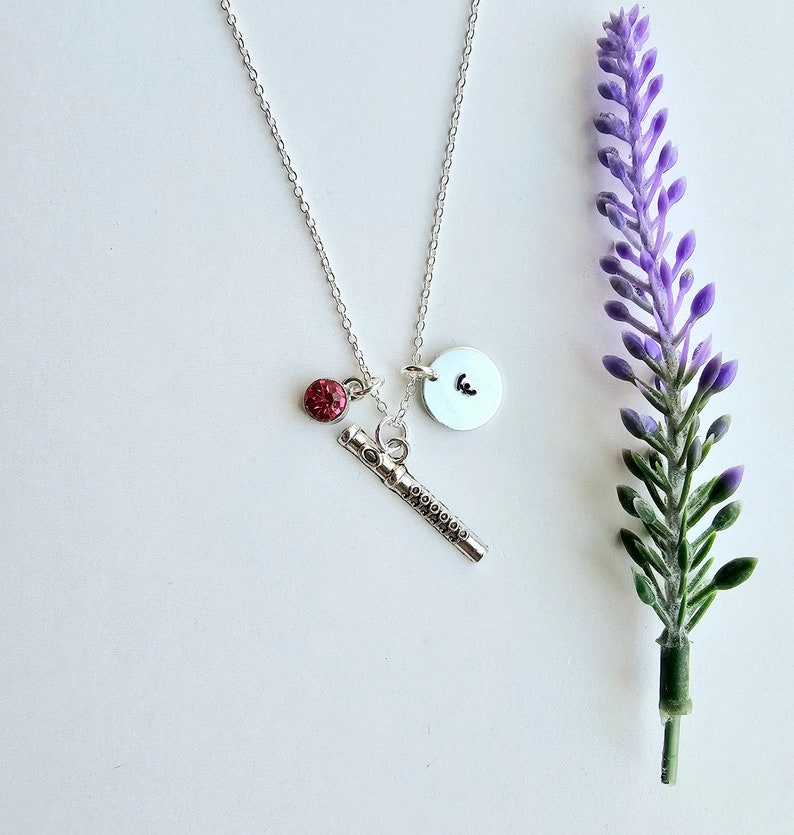 May include: A silver necklace with a silver flute charm, a small red rhinestone charm, and a silver disc charm with the letter "E" on it.