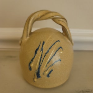 May include: A small, beige ceramic pitcher with a twisted handle and blue brushstrokes.