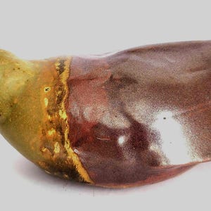 May include: A ceramic bird figurine with a green head and a brown body. The bird has a small beak and a rounded body. The colors blend together, creating a unique and artistic appearance. The figurine is likely a decorative item.