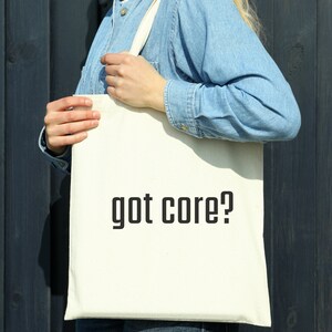 Puede incluir: Una bolsa de tela blanca con texto negro que dice "got core?" La bolsa está siendo sostenida por una persona que lleva una camisa vaquera azul.