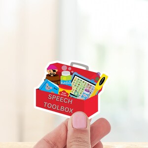 May include: A red toolbox with a white outline and the words "Speech Toolbox" on the front. The toolbox is open and filled with various items, including a book, play dough, bubbles, a toy pirate, and a yellow ruler.