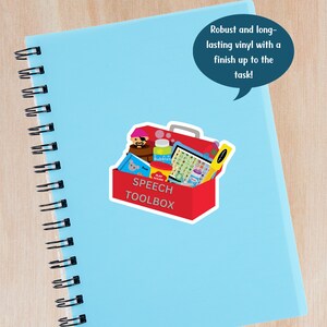 A sticker that says speech toolbox is on a blue spiral notebook.  The image includes a red toolbox with various speech therapy toys and tools.