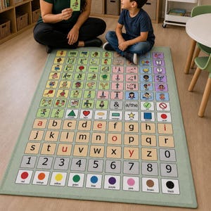 K&ouml;nnte beinhalten: Ein rechteckiger Lernteppich mit hellgr&uuml;nem Rand. Der Teppich zeigt ein Raster aus farbigen Quadraten mit Buchstaben, Zahlen und Symbolen. Der Teppich hat auch Illustrationen und W&ouml;rter. Eine Person und ein Kind sitzen in der N&auml;he des Teppichs.