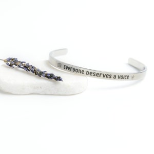 May include: A silver bracelet with the inscription "Everyone deserves a voice" and a small symbol of a square with a line through it.
