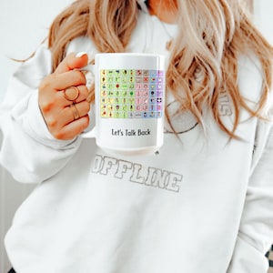 May include: White ceramic mug featuring a colourful grid of ASL signs and the text "Let's Talk Back".