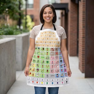 Puede incluir: Delantal blanco con una correa negra para el cuello, con una colorida cuadrícula de símbolos y letras. El delantal tiene un diseño tipo teclado en la parte superior, con números y puntos de colores en la parte inferior. El delantal lo lleva una persona.