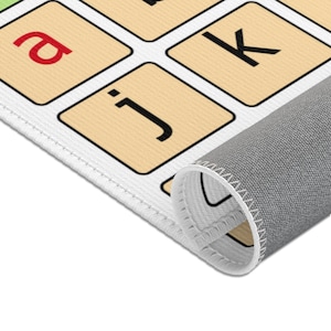 An AAC core vocabulary rug is on white floor.  The edge of the AAC carpet is shown.