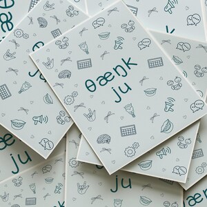 A flat lay image of multiple SLP-themed greeting cards with the phrase “θæŋk ju” written in IPA. Surrounded by doodles of speech therapy-related visuals like speech bubbles, ASL hands, AAC icons, and vocal tracts. Ready-to-print digital download format.