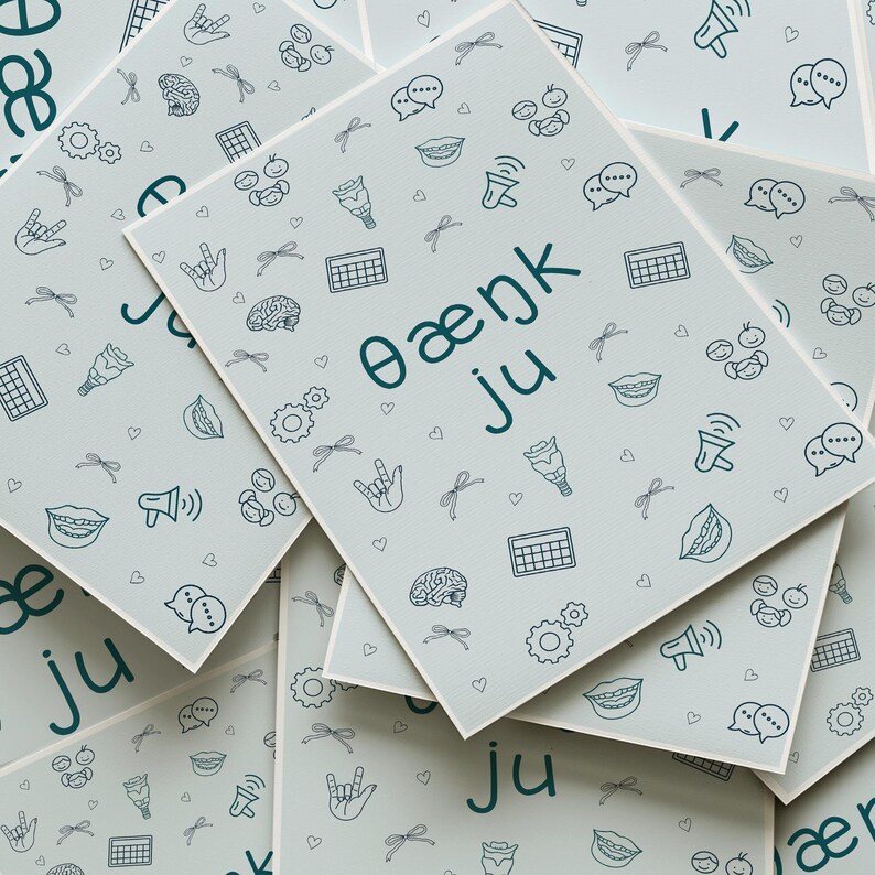 A flat lay image of multiple SLP-themed greeting cards with the phrase “θæŋk ju” written in IPA. Surrounded by doodles of speech therapy-related visuals like speech bubbles, ASL hands, AAC icons, and vocal tracts. Ready-to-print digital download format.