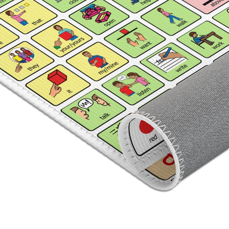 An AAC core vocabulary rug is on white floor.  The edge of the AAC carpet is shown.