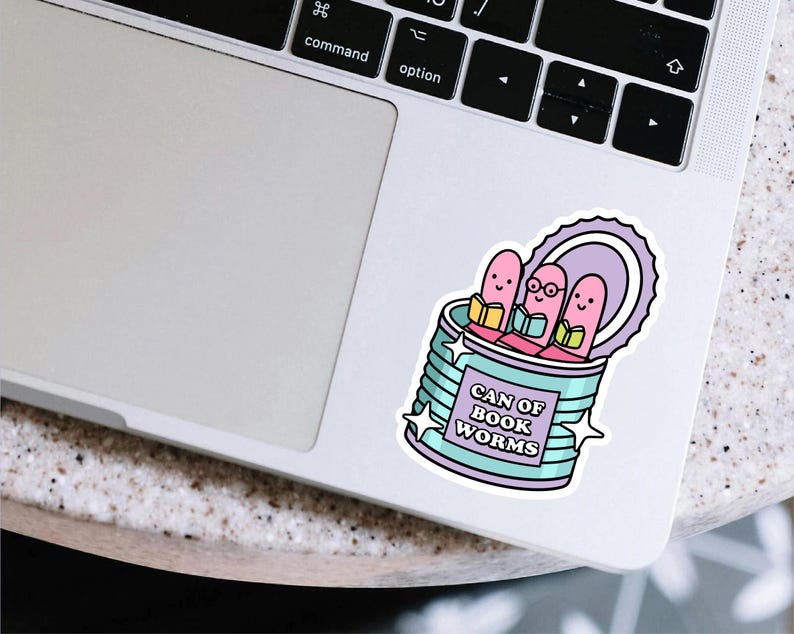 May include: A sticker featuring a whimsical design of three pink bookworms reading inside a teal can. The can is labeled "CAN OF BOOK WORMS" in purple text, with star accents. The sticker is placed on a laptop.