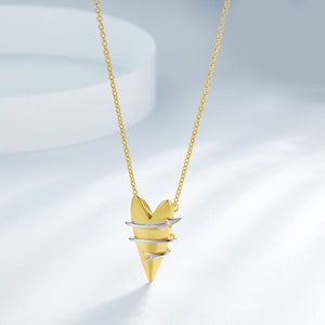 May include: A gold heart pendant necklace with a silver wire design wrapped around it. The necklace has a delicate chain.