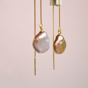 May include: A pair of gold chain earrings with a large, irregular shaped, iridescent pearl pendant on each earring.