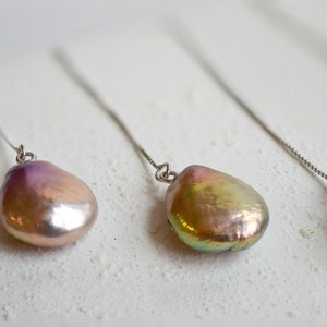 May include: Three pairs of dangle earrings with iridescent pink and gold pearls hanging from thin silver chains.