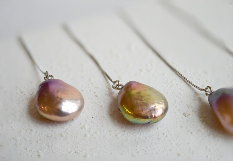 May include: Three pairs of dangle earrings with iridescent pink and gold pearls hanging from thin silver chains.