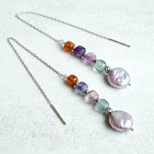 May include: A pair of silver chain earrings with a mix of orange, purple, green, and white gemstone beads and a large pearl drop.