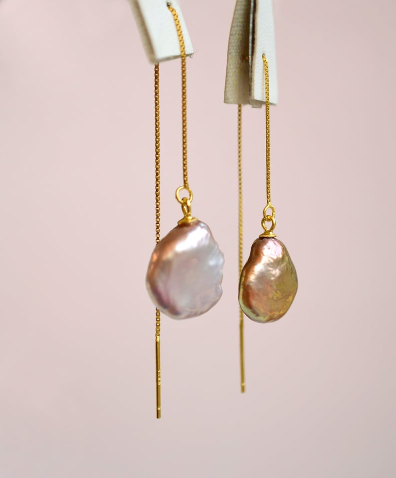 May include: A pair of gold chain earrings with a large, irregular shaped, iridescent pearl pendant on each earring.