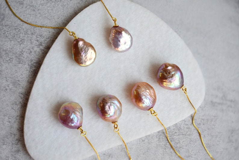 May include: Five iridescent pink and gold pearl pendants on delicate gold chains. The pearls are various shapes and sizes.