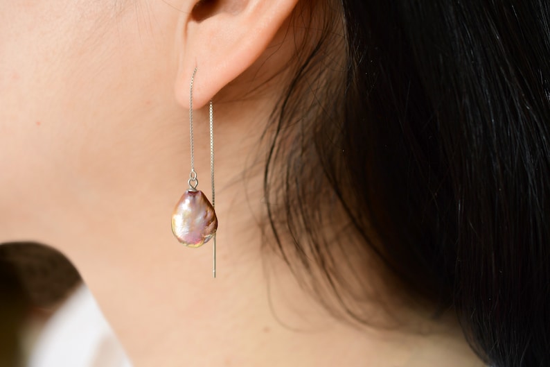 May include: A pair of silver dangle earrings with a single iridescent purple pearl drop on each earring.