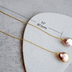 May include: A pair of gold chain earrings with a pink pearl drop. The earrings are 3.5 inches long and the pearls are 13mm in diameter.