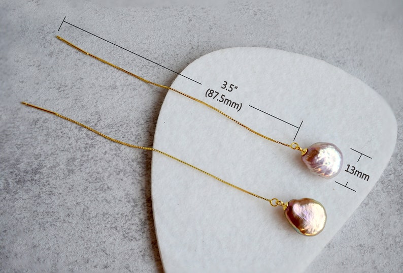 May include: A pair of gold chain earrings with a pink pearl drop. The earrings are 3.5 inches long and the pearls are 13mm in diameter.