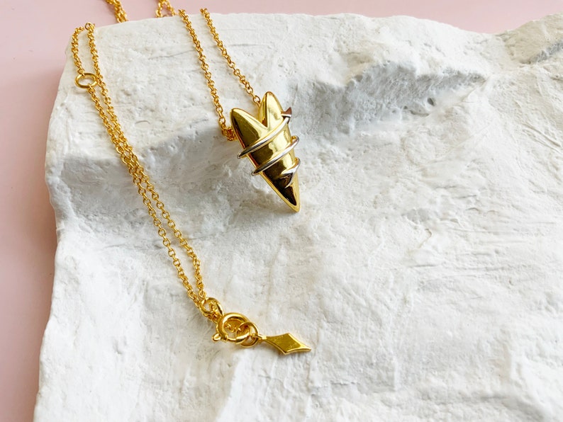 May include: A gold necklace with a heart-shaped pendant. The pendant is made of two different metals, one gold and one silver, and is twisted together to create a unique design.
