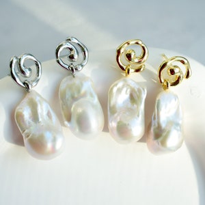 May include: Two pairs of drop earrings featuring irregular, lustrous white baroque pearls suspended from metallic swirl-shaped studs. One pair is finished in a bright silver tone, while the other pair is finished in a polished gold tone.