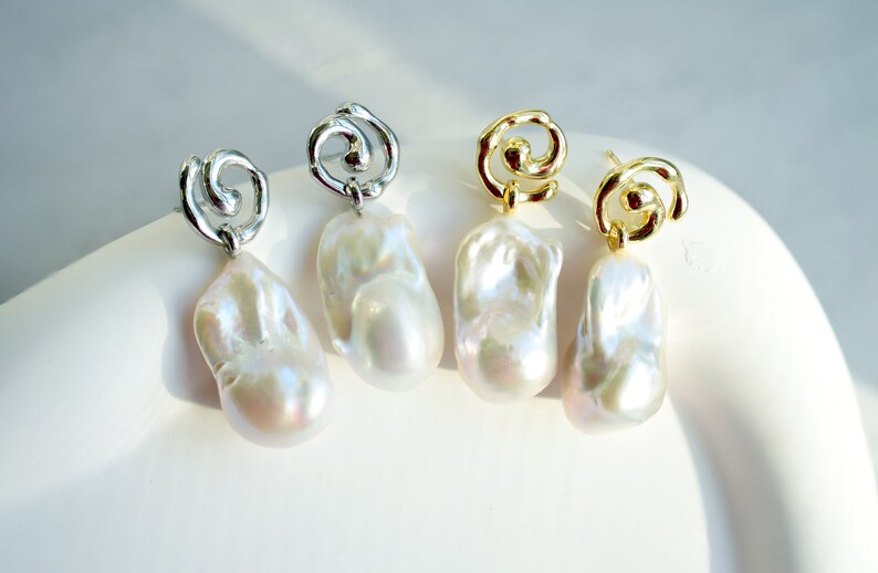 May include: Two pairs of drop earrings featuring irregular, lustrous white baroque pearls suspended from metallic swirl-shaped studs. One pair is finished in a bright silver tone, while the other pair is finished in a polished gold tone.