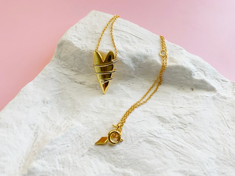 May include: A gold necklace with a heart pendant. The heart is made of twisted wire and has a delicate, intricate design.