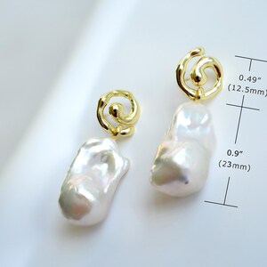 May include: A pair of gold-tone earrings featuring irregular white baroque pearls suspended from swirling metal loops. The top loop measures 0.49 inches and the pearl drop measures 0.9 inches in length as indicated by the measurement markers.