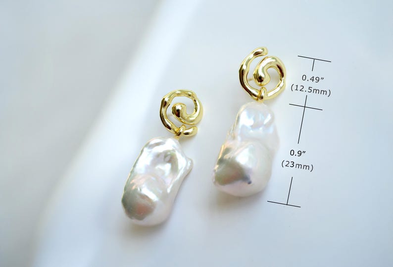 May include: A pair of gold-tone earrings featuring irregular white baroque pearls suspended from swirling metal loops. The top loop measures 0.49 inches and the pearl drop measures 0.9 inches in length as indicated by the measurement markers.