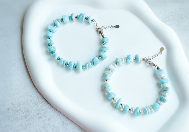 Puede incluir: Dos pulseras con cuentas de piedra azul claro, irregulares y pulidas. Una pulsera incluye peque&ntilde;as cuentas espaciadoras de color turquesa, mientras que la otra presenta perlas blancas de forma ovalada. Ambas tienen cierres y cadenas de metal plateado.