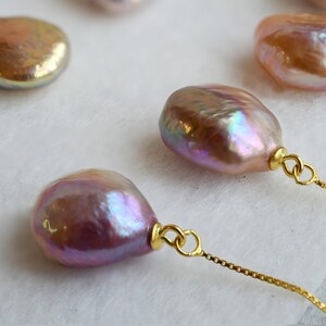 May include: Four iridescent baroque pearls with gold accents on a gold chain. The pearls are a light pink color with a pearlescent sheen.