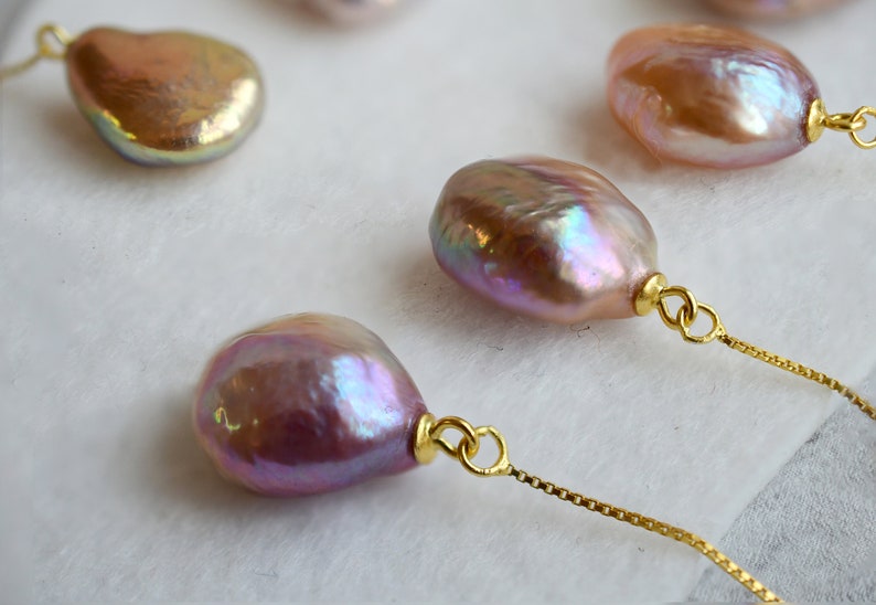 May include: Four iridescent baroque pearls with gold accents on a gold chain. The pearls are a light pink color with a pearlescent sheen.