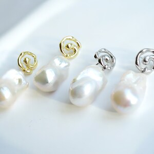 May include: Two pairs of drop earrings featuring irregular, lustrous white baroque pearls suspended from metallic swirl-shaped studs. One pair is finished in a bright gold tone, while the other pair is finished in a polished silver tone.
