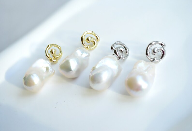 May include: Two pairs of drop earrings featuring irregular, lustrous white baroque pearls suspended from metallic swirl-shaped studs. One pair is finished in a bright gold tone, while the other pair is finished in a polished silver tone.
