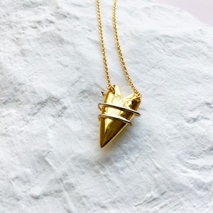 May include: A gold necklace with a heart-shaped pendant. The pendant is made of two pieces of metal, one gold and one silver, that are intertwined. The necklace is on a white background.