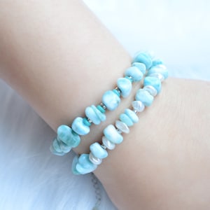 Puede incluir: Una pulsera de doble hilo con piedras de larimar azul claro pulidas e irregulares, intercaladas con peque&ntilde;as perlas blancas y diminutas cuentas de metal plateado. Las piedras tienen una textura suave y est&aacute;n dispuestas en patr&oacute;n.