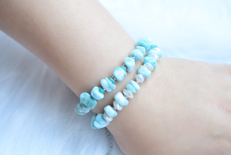 Puede incluir: Una pulsera de doble hilo con piedras de larimar azul claro pulidas e irregulares, intercaladas con peque&ntilde;as perlas blancas y diminutas cuentas de metal plateado. Las piedras tienen una textura suave y est&aacute;n dispuestas en patr&oacute;n.