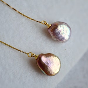 May include: A pair of gold chain earrings with a large, iridescent pink pearl on each end.