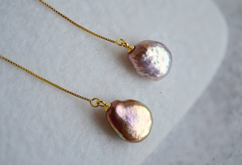 May include: A pair of gold chain earrings with a large, iridescent pink pearl on each end.