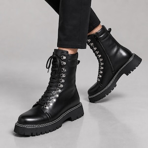 May include: Black mid-calf boots featuring a lace-up front with silver-toned metal eyelets, a side zipper closure, a padded collar, and a thick, lugged rubber sole with prominent white contrast stitching along the welt of the boot.
