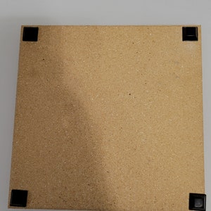 May include: A light brown rectangular cork board with black rubber feet on each corner.