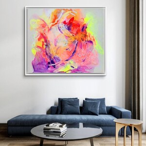 May include: Abstract painting with vibrant colors, including pink, orange, yellow, and purple. The painting is framed in a white frame and is hanging on a white wall.