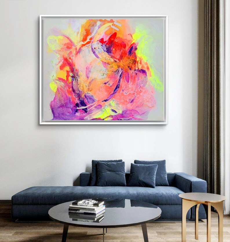 May include: Abstract painting with vibrant colors, including pink, orange, yellow, and purple. The painting is framed in a white frame and is hanging on a white wall.