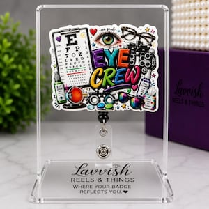 May include: A badge reel featuring a colorful graphic with the text EYE CREW, an eye chart, an eye illustration, glasses, and optical tools. The reel is mounted on a clear acrylic stand with the text Lavvish REELS & THINGS WHERE YOUR BADGE REFLECTS YOU.