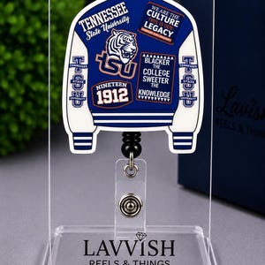 May include: A blue and white varsity jacket shaped badge reel featuring the Tennessee State University tiger logo, the text "We Are The Culture This Is Our Legacy", "Nineteen 1912", and "Blacker The College Sweeter The Knowledge" on a clear acrylic stand.