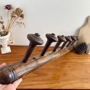 May include: A vintage wooden coat rack with six pegs. The rack is made of dark brown wood and has a slightly curved shape. The pegs are mushroom-shaped. The rack is displayed on a wooden table.