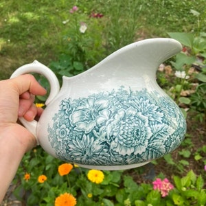 May include: A white ceramic pitcher with a green floral design. The pitcher has a wide mouth and a handle.